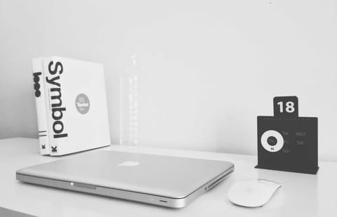 Bureau blanc en noir et blanc: un ordinateur portable fermé, deux livres debout, une souris et un calendrier de bureau. Rien d’autre.